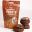 A stand-up pouch of Go bake Choccy Toppys (choc pearls) next to three chocolate chip cookies topped with the white and beige chocolate pearls, on a clean white background.