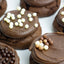 Chocolate sandwich cookies with smooth chocolate frosting, decorated with white chocolate sprinkles and chocolate pearls on a light background.