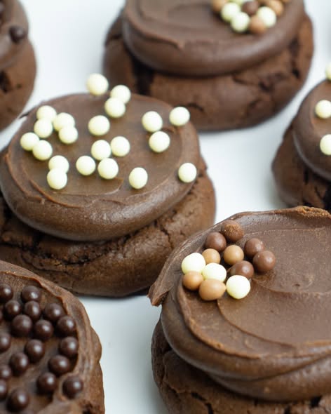 Chocolate sandwich cookies with smooth chocolate frosting, decorated with white chocolate sprinkles and chocolate pearls on a light background.