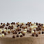 A close-up of a brown frosted cake topped with scattered chocolate and white chocolate candies against a light gray background.
