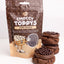 A 100g stand-up pouch of GoBake Choccy Toppys Choc Pearsls next to three stacks of chocolate chip cookies on a white background.