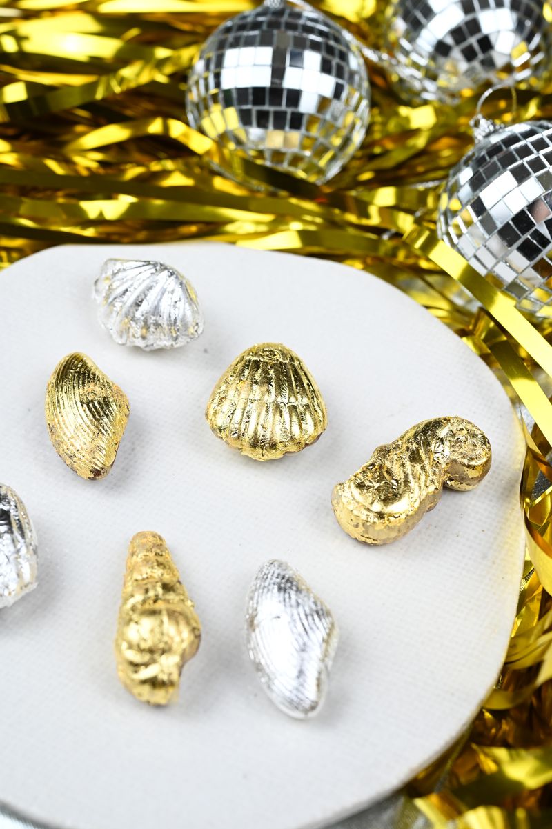 Gold and silver shell-shaped chocolates on a white surface with disco balls and tinsel in the background.