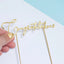 Gold 'Congratulations' cake topper held by a hand on a light blue and white background