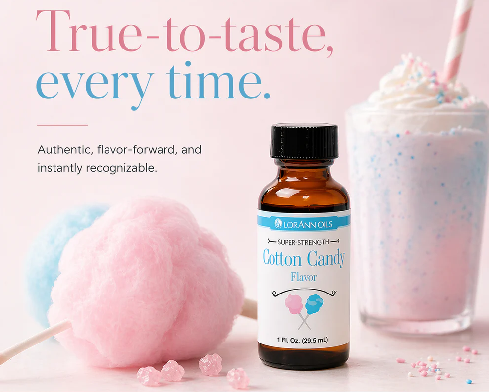 A bottle of LorAnn Oils cotton candy flavor essential oil centered in a styled product photo with pink and blue cotton candy, a pink milkshake, and promotional text on a soft pink background.