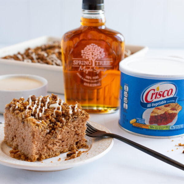 Slice of cake with Crisco shortening container and Spring Tree maple syrup bottle on a white surface.