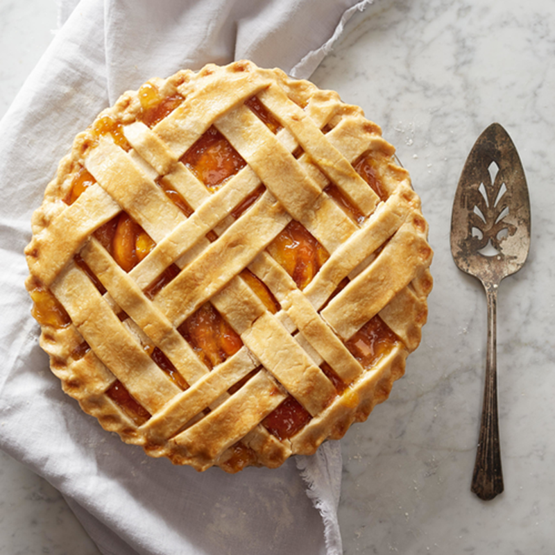 Peach pie with a lattice crust on a marble surface with a pie server.