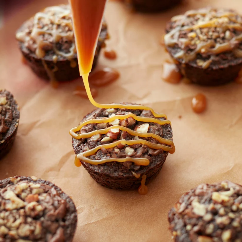 small muffins topped with nuts, being drizzled with caramel