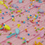 Close-up of pink frosted cake or pastry topped with colorful candy sprinkles and pastel candy pieces.