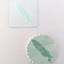 A clear debosser tool with a feather design, placed on a white surface. Alongside an range cookie made using the tool