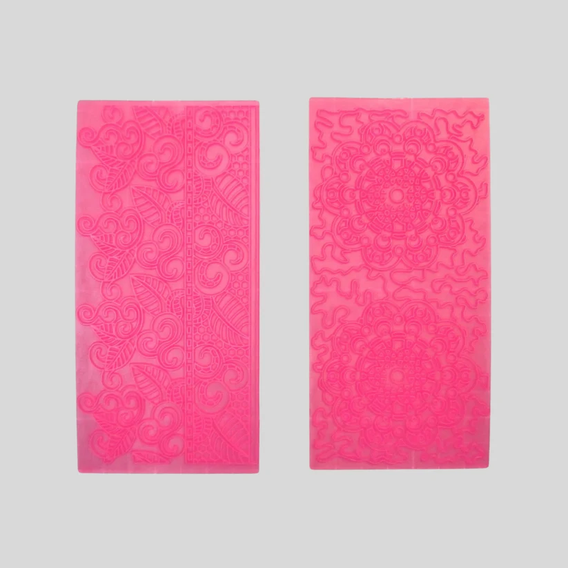 Two rectangular impression mats for fondant icing in a vibrant hot pink color, displayed side-by-side against a neutral light gray background. The left die features an intricate floral and scroll pattern, while the right die showcases a mandala design.