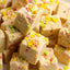 Close-up of cubed beige fudge or candy pieces topped with colorful sprinkles, filling the frame.