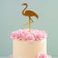 Small cake with pink flowers and a gold flamingo topper on a light blue background