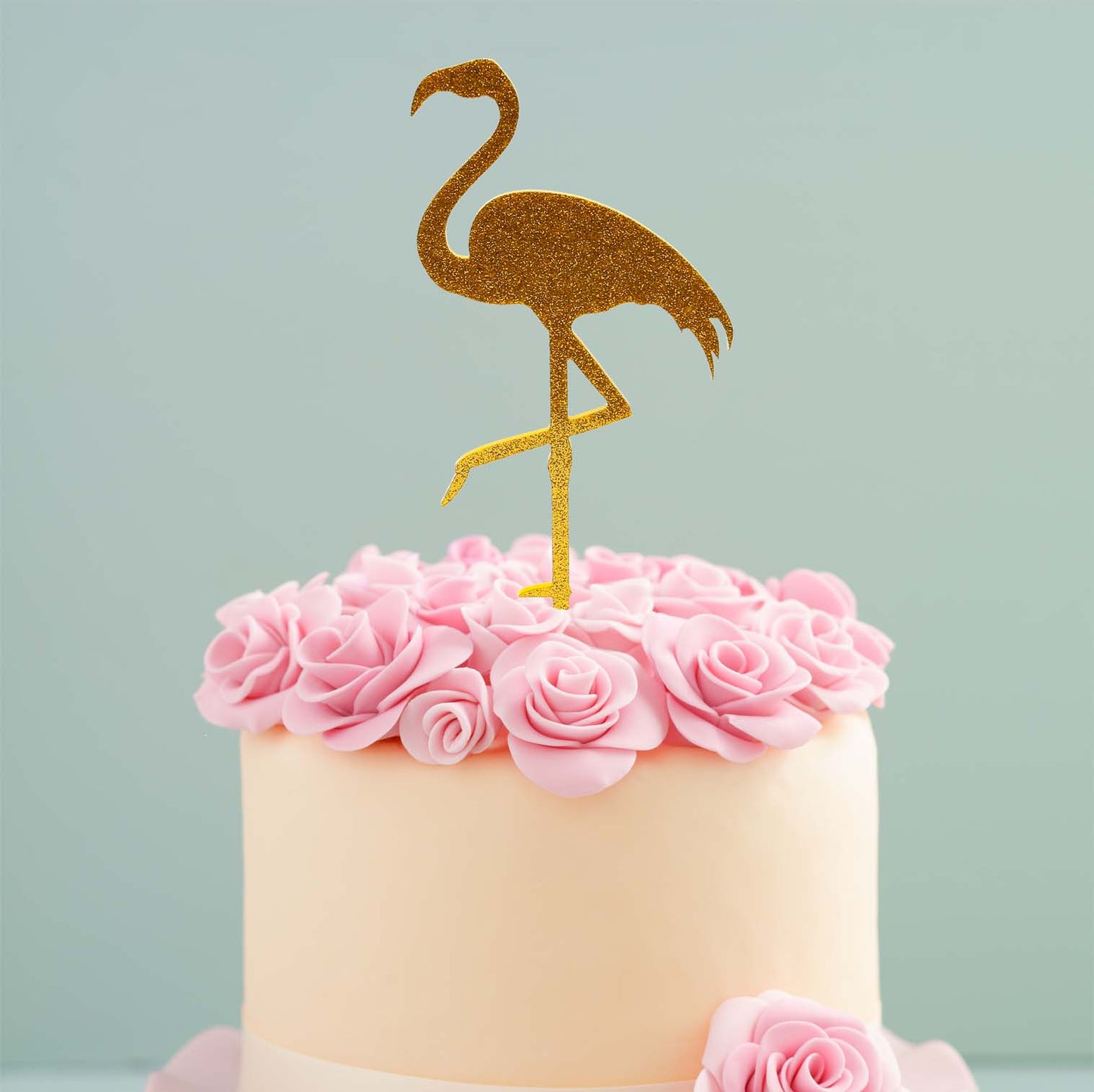 Small cake with pink flowers and a gold flamingo topper on a light blue background