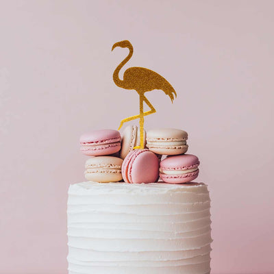 Small cake with pink macarons and a gold flamingo topper on a light pink background