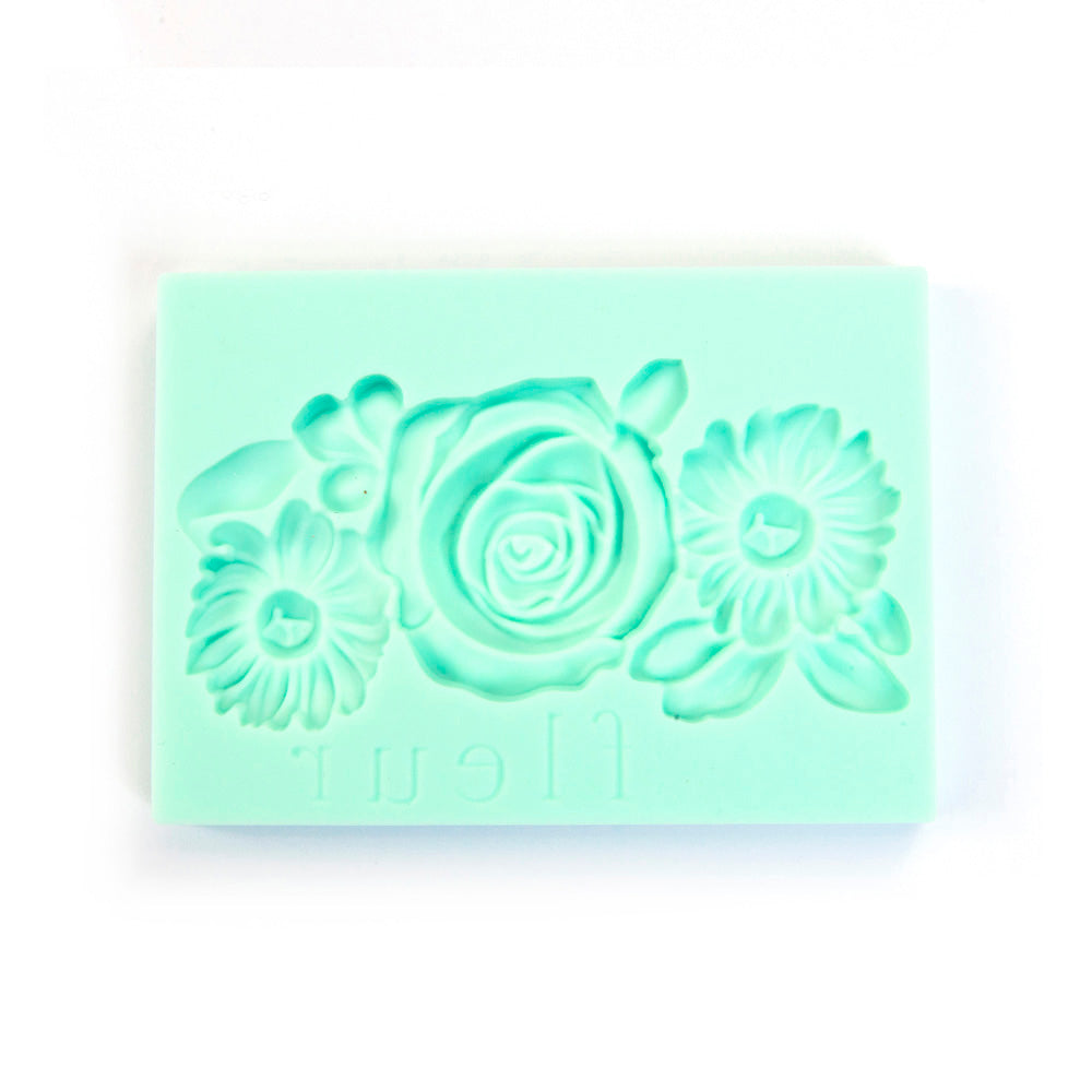 A mint green rectangular silicone mold with embossed floral designs, including a central rose and two daisies, on a plain white background.