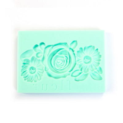 A mint green rectangular silicone mold with embossed floral designs, including a central rose and two daisies, on a plain white background.