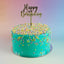 A round birthday cake with bright turquoise frosting, decorated with multicolored star-shaped sprinkles and topped with a gold 'Happy Birthday' script topper, set against a soft pastel gradient background.