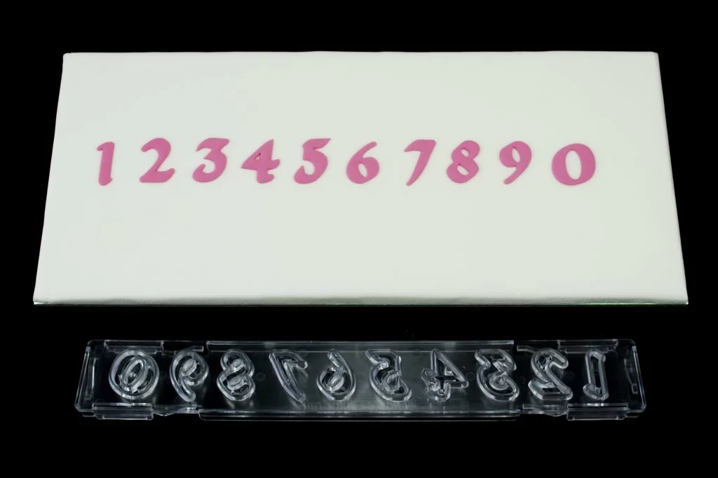 A set of clear plastic number cutters laid out next to their corresponding fondant icing number on a white background.
