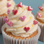 Cupcake with white frosting and pink heart decorations on a light blue background