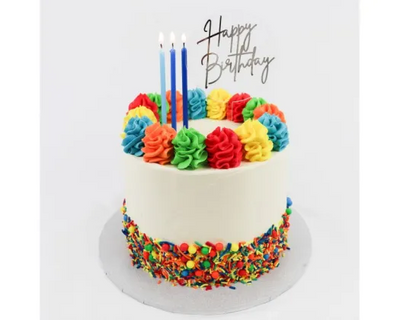 A round birthday cake with white frosting, decorated with colorful piped rosettes around the top edge, multicolored sprinkles around the base, three blue candles, and a 'Happy Birthday' script topper on a white background.