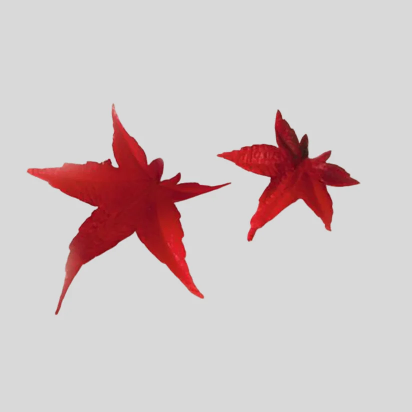 Two red gumpaste icing maple leaf decorations on a plain light gray background.
