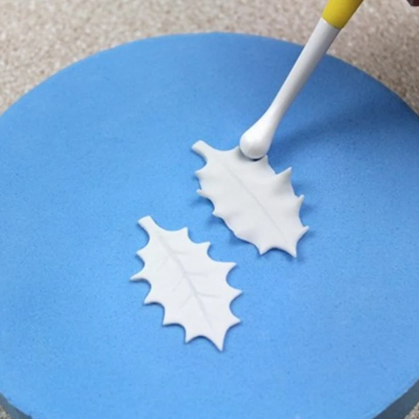 2 icing holly leaves on a flower shaping foam pad. With a modelling tool