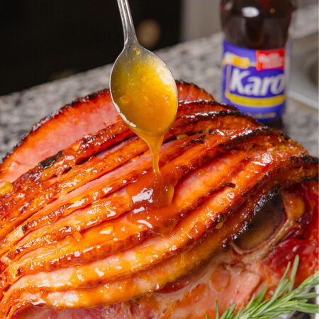 Sliced ham with a spoon drizzling glaze over it, Karo syrup bottle in the background.