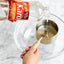 Person pouring Karo corn syrup into a measuring cup with a glass bowl in the background.