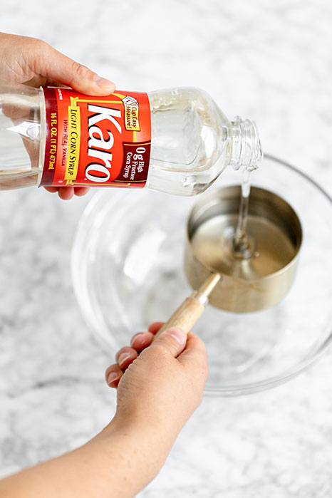 Person pouring Karo corn syrup into a measuring cup with a glass bowl in the background.