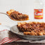 Pecan pie with a slice being lifted on a metal spatula, with a jar of Karo in the background.
