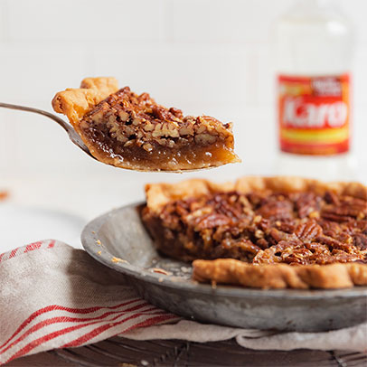 Pecan pie with a slice being lifted on a metal spatula, with a jar of Karo in the background.