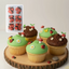 Decorative cupcakes with green icing, brown chocolate, and red ladybug decorations on a wooden board.