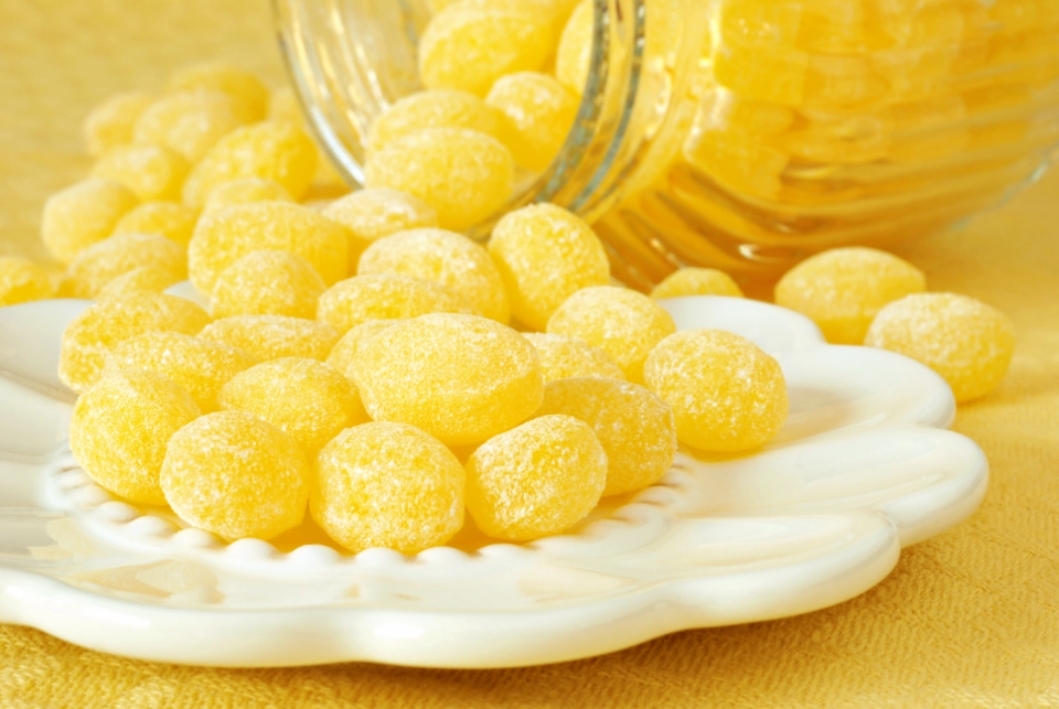 Yellow lemon flavoured hard candies on a white plate with a jar in the background