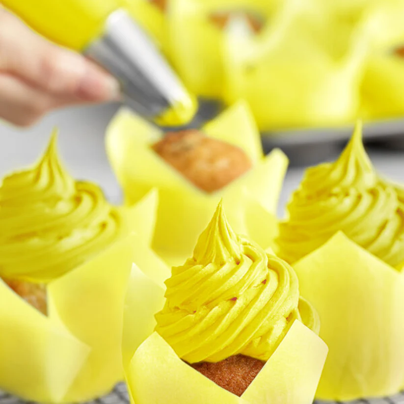 Person frosting yellow cupcakes with a piping bag.