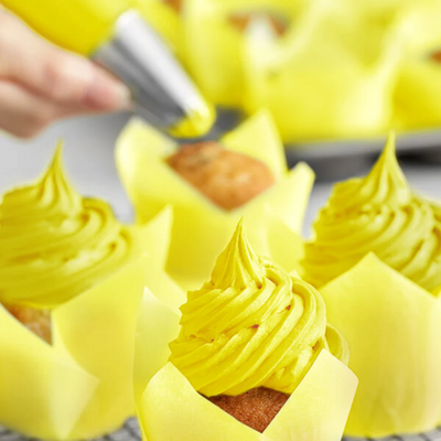Person frosting yellow cupcakes with a piping bag.