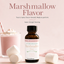 An amber glass bottle of Lorann Marshmallow Flavor Super Strength flavoring, styled on a soft pink background with a pink drink, whipped cream, and marshmallows.