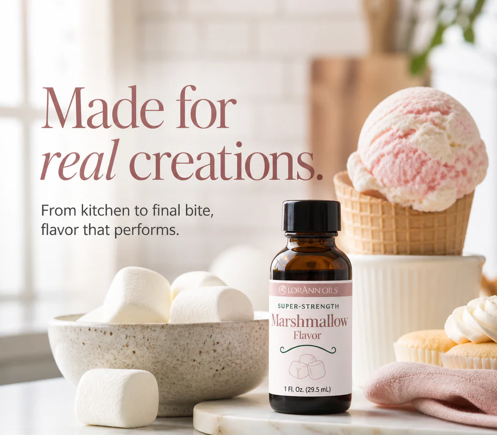 A bottle of Lorann Super-Strength Marshmallow Flavor is displayed on a marble surface with marshmallows, ice cream, and cupcakes in a bright kitchen setting. Text on the left reads 'Made for real creations.