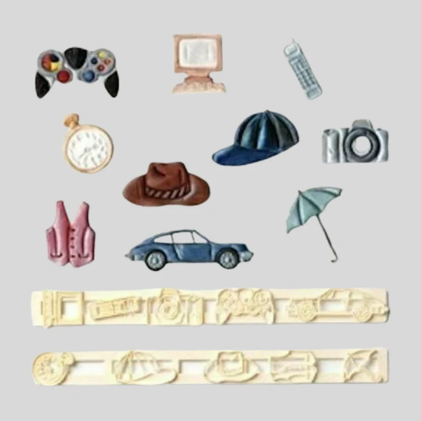 A set of fondant icing decorations arranged on a light gray background, including a game controller, computer monitor, phone, pocket watch, camera, hat, car, umbrella, alongside the cutter set used to make them