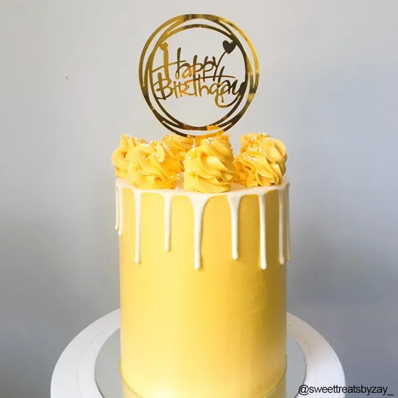Yellow birthday cake with floral decorations and a 'Happy Birthday' topper on a gray background.