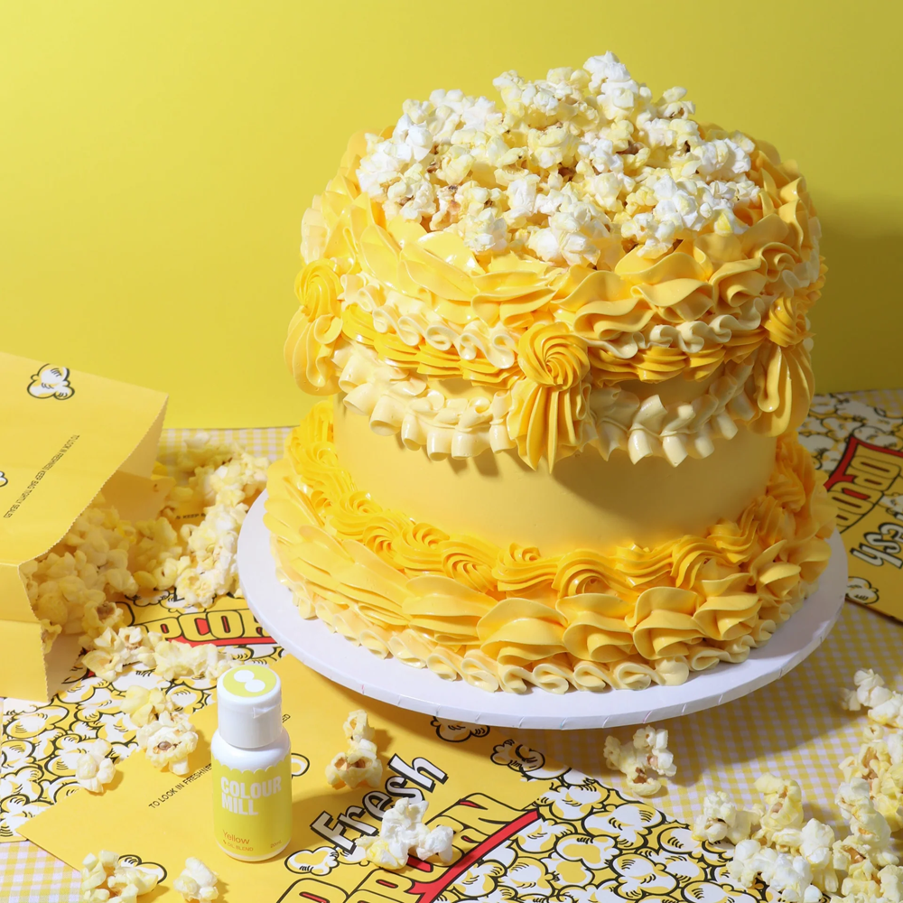 Two-tiered yellow cake with popcorn on top against a yellow background