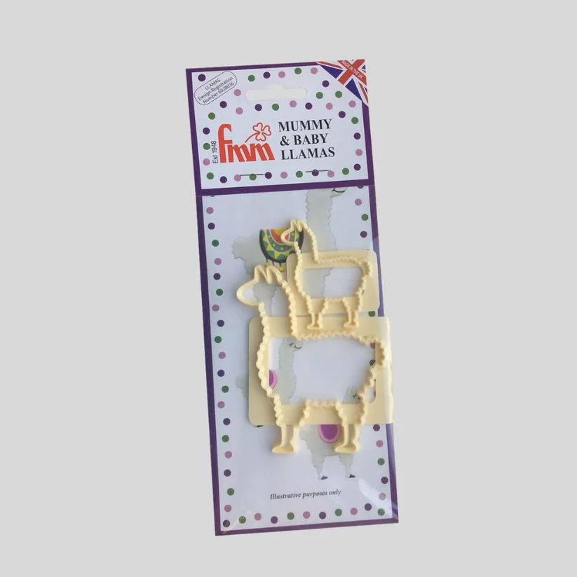 A pale yellow plastic cutter shaped like a mummy and baby llama, still in its original retail packaging card, shown against a solid gray background. By FMM
