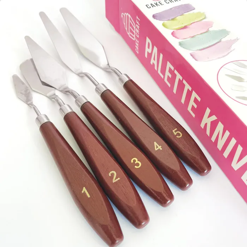 Set of palette knives with brown handles and metal blades, displayed in front of a pink packaging box.