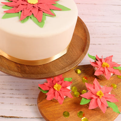 Decorative cake with red and green poinsettia floral decorations on a wooden stand