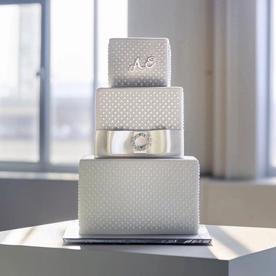 Three-tiered silver wedding cake with decorative elements on a white surface.