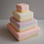Stack of four square, pastel-colored cakes with textured surfaces on a gray background