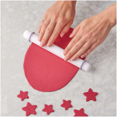 Person using a rolling pin to shape red fondant on a gray surface with star-shaped decorations.