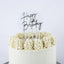 A round white frosted cake with piped cream frosting rosettes around the top edge, featuring a clear circular 'Happy Birthday' cake topper with black script lettering.