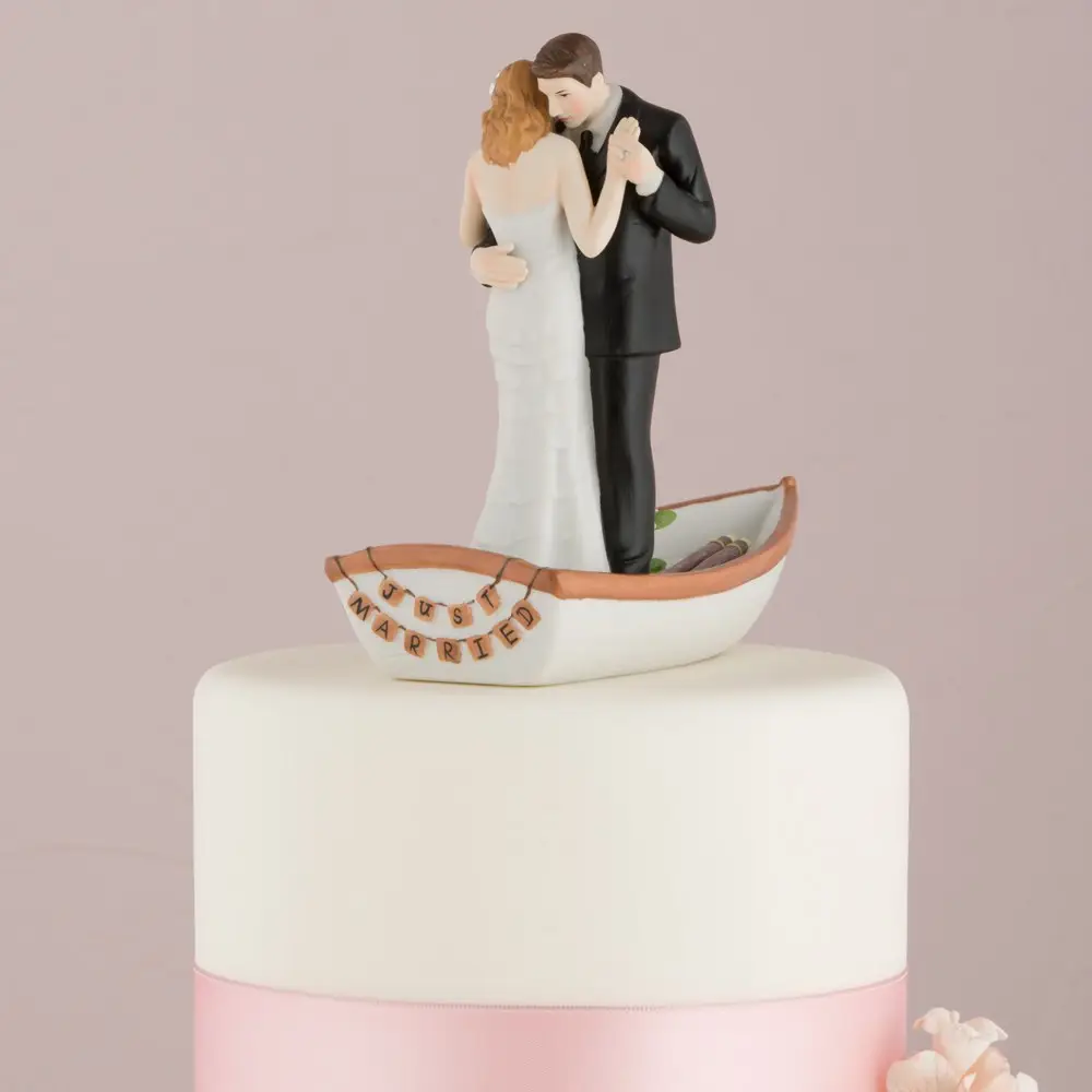 Wedding cake topper with bride and groom on a boat against a pink background