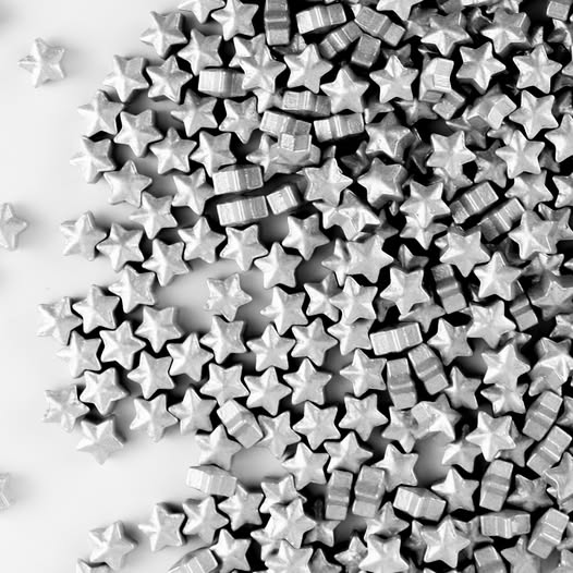 A pile of small metallic silver star-shaped sprinkles scattered across a plain white background.