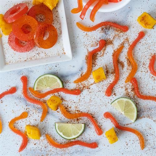 Worm gummy candies with lime wedges and spicy chilli powder on a white bench top